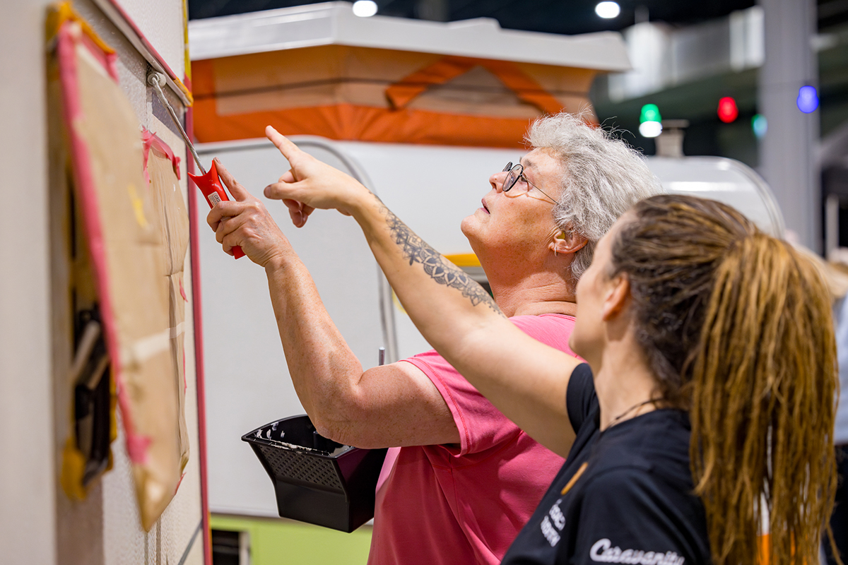 vrouw geeft aanwijzingen hoe andere vrouw caravan moet schilderen