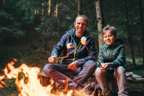 ather and son roast marshmallow candies on the campfire in forest. Spring or autumn camping