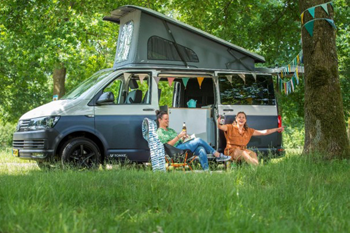Twee kampeerders genieten voor een campervan onder de bomen, versierd met vlaggetjes.