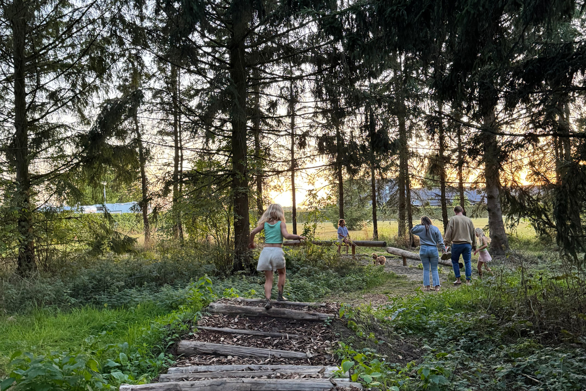 Kinderen en volwassenen lopen over het blotevoetenpad door het bos bij Buitengoed de Boomgaard