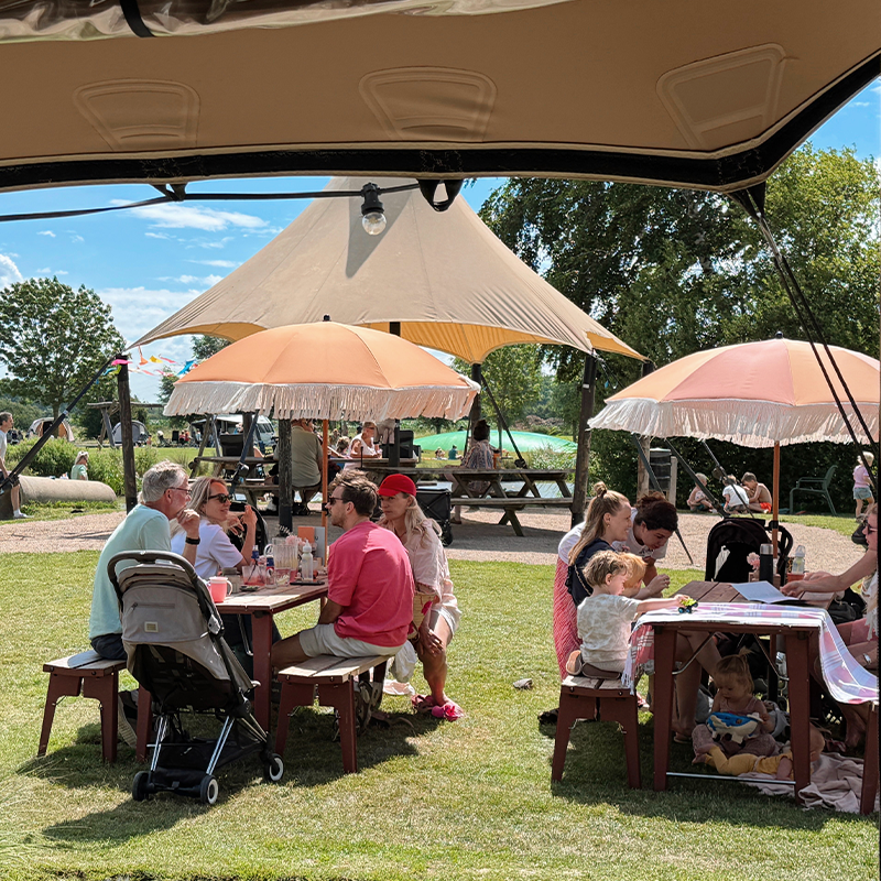Pluk je buitengeluk mensen aan picknick tafels met parasol